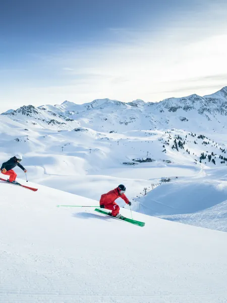 Schneesicherheit Zwei Skifahrer fahren eine präparierte Piste in einem alpinen Skigebiet hinunter